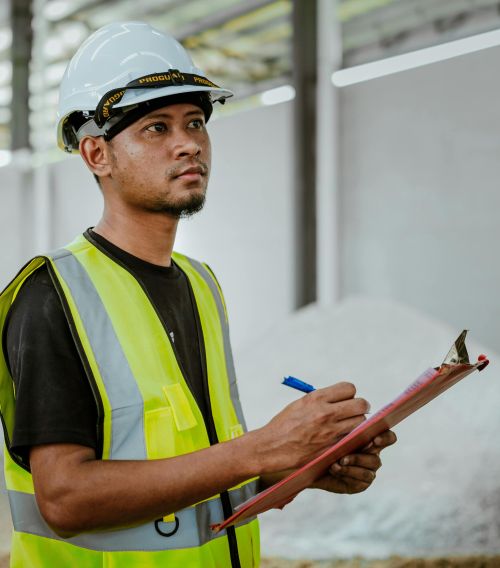 Asian construction worker in a factory setting, using a clipboard for inspection tasks in Banting, Malaysia.