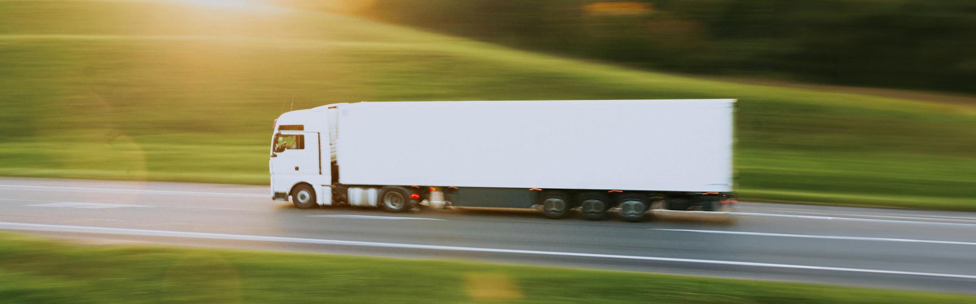 White cargo truck speeding through Vitebsk countryside at sunrise, symbolizing transportation and logistics.