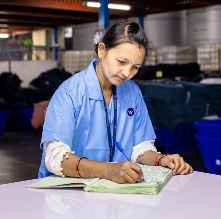 Woman in blue uniform taking notes in an industrial warehouse setting.