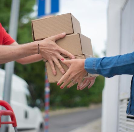 Hands exchanging cardboard boxes during an outdoor delivery scene.